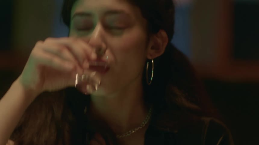 Shot glasses lined up and a woman taking a shot squinting her face