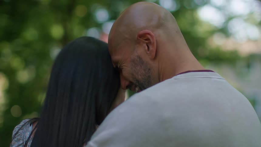 A man and woman smiling and holding each other while another person jumps in the background