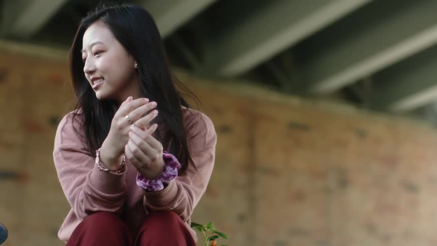 Woman sits under structure and smiles while looking over to see what friend is doing