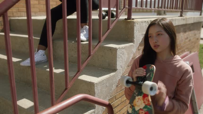 A women sitting on a skateboard on steps while another girl stands and then walks up the steps
