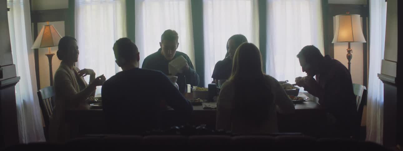 A group of people sitting around a table eating then two men stand up from the table and walk away