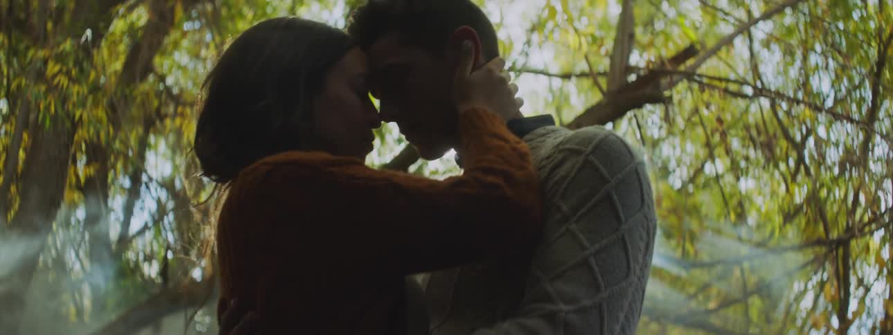 Two lovers hugging and caressing eac hother in the forest sunlight shining on them through the trees