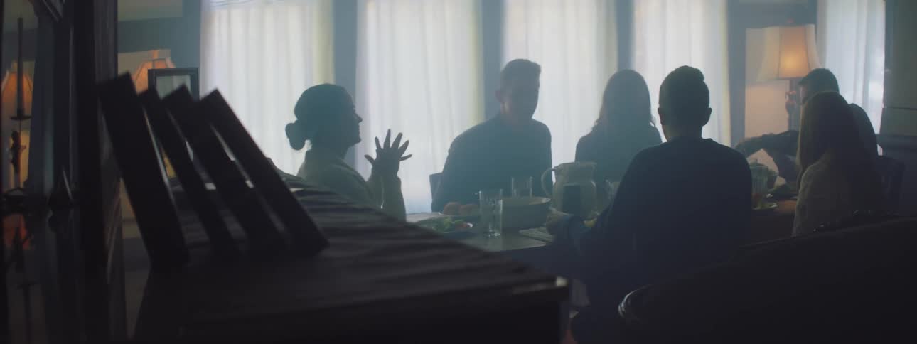 A group of friends sits at dining table near piano in room
