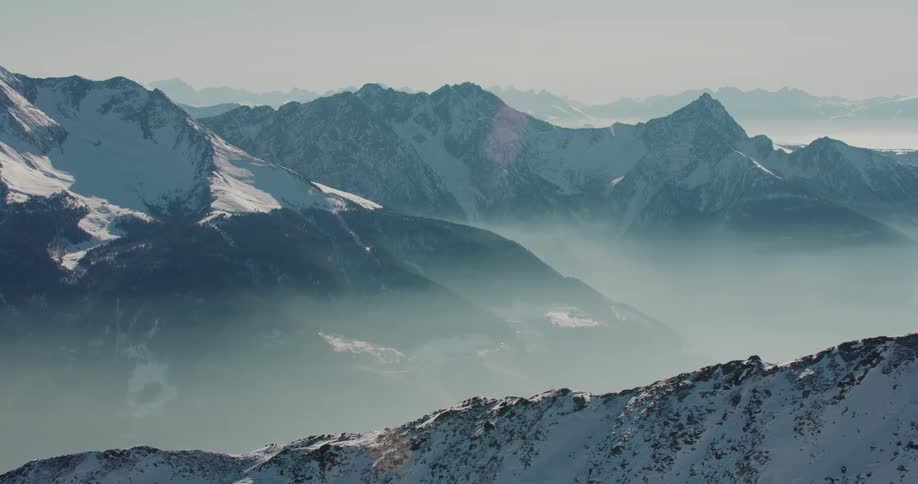 A mountain range covered in snow and fog during the day