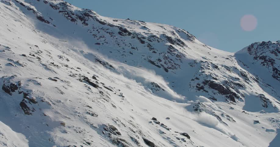 Snow covers the rough terrain of a mountainside during an avalanche under a clear blue sky