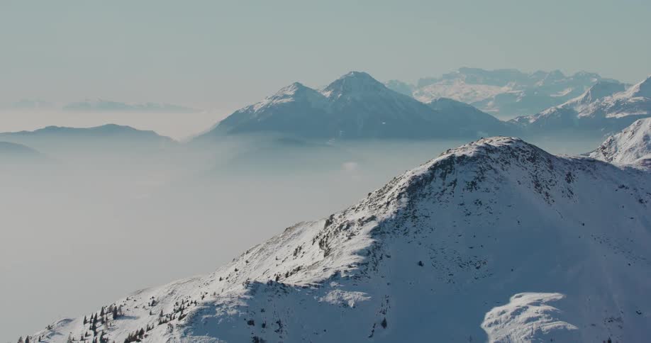 An aerial view of snow covered mountain peaks with fog settling in the valley