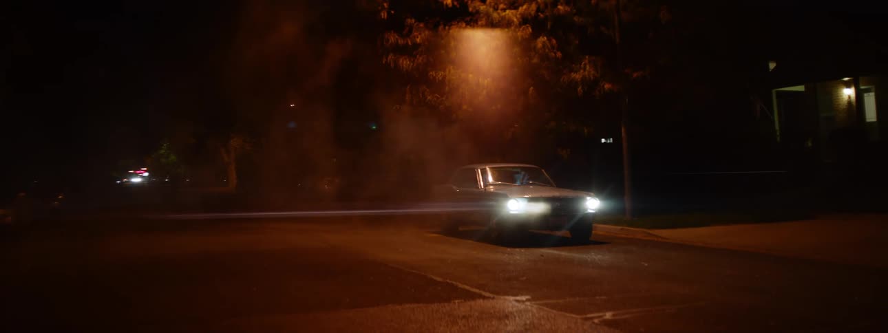 A vehicle sits parked in a poorly lit parking lot at night
