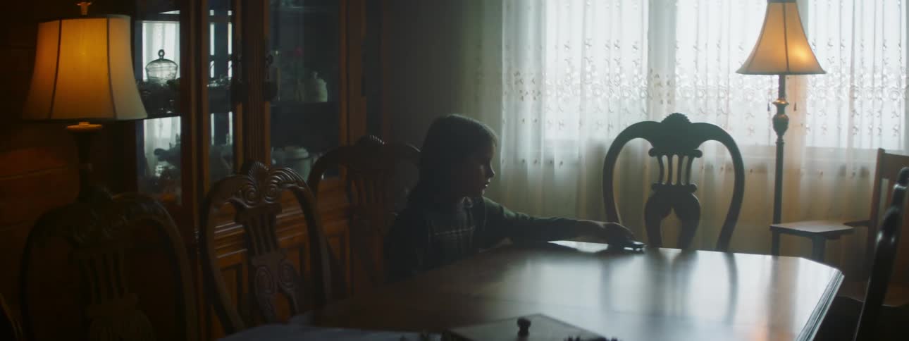 A girl is sitting at the dining room table playing with a car as she pushes it across the table top