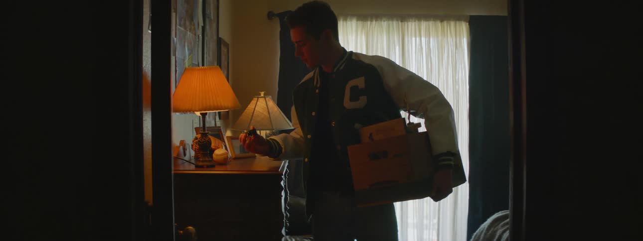 Man with green and white jacket gets out of room carrying a box with stuff and touches toy car