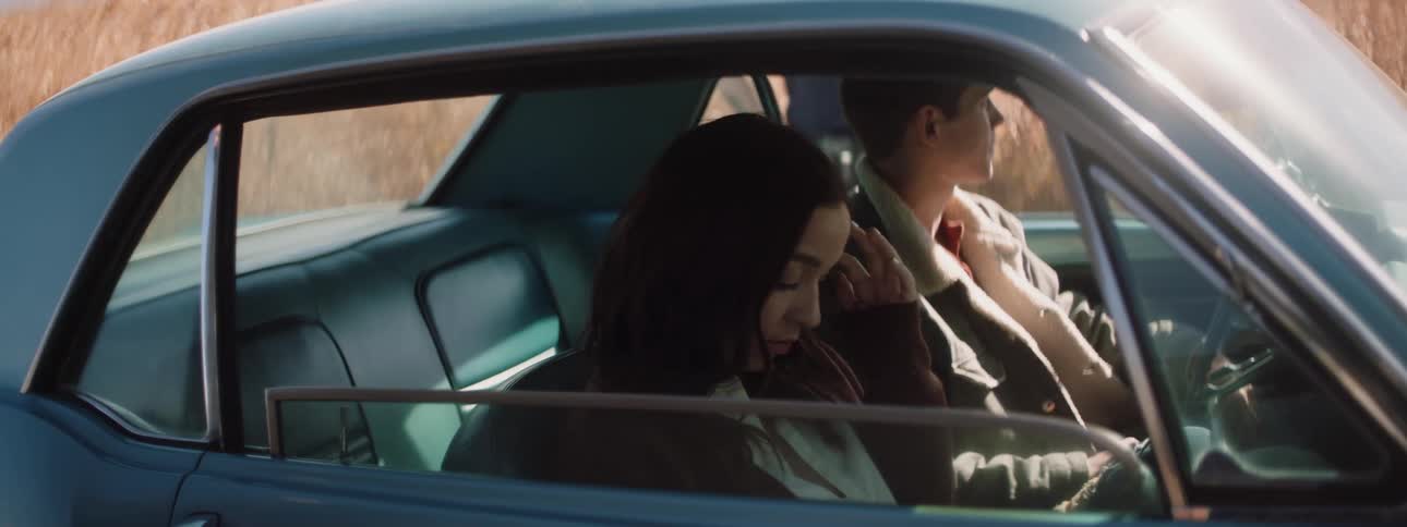 A young couple sit nervously in a car waiting for an approaching police officer during the daytime in a rural location