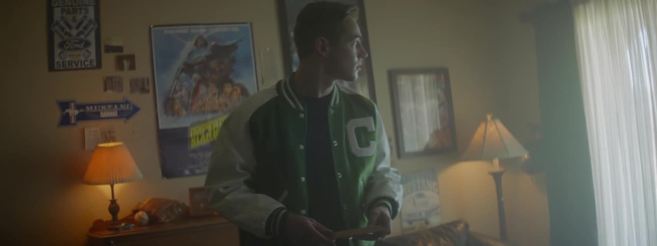 Man wearing letter jacket packs things into a box in bedroom