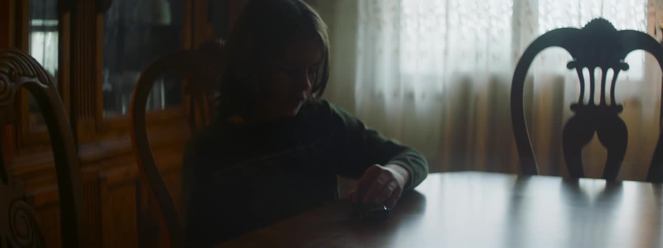 Child with sweatshirt sits at dining table and plays with toy car in room