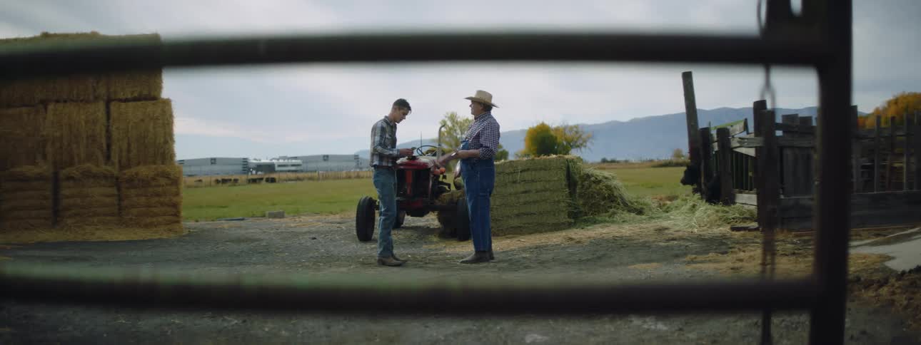 A farmer pays a man standing in front of him and then they shake hands and walk away