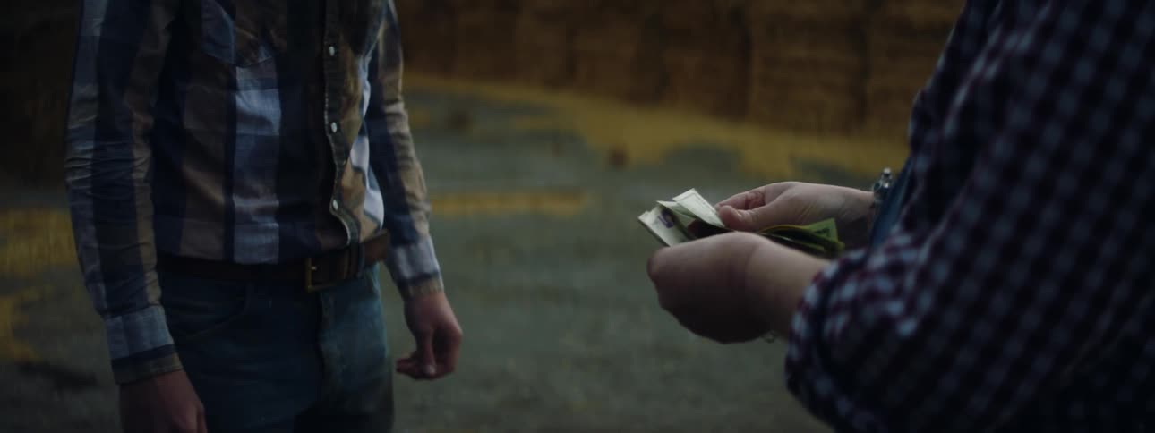 Farmer standing near walls made from stacked hay bales pays young man in cash