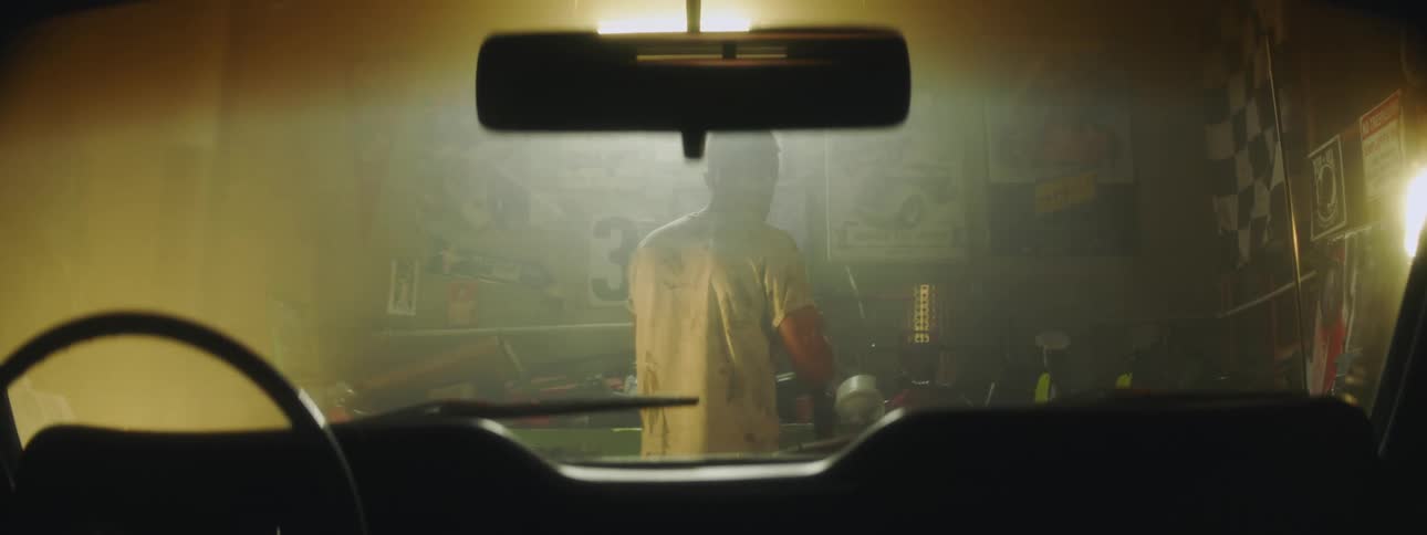 Man standing in front of car in garage uses tools from workbench