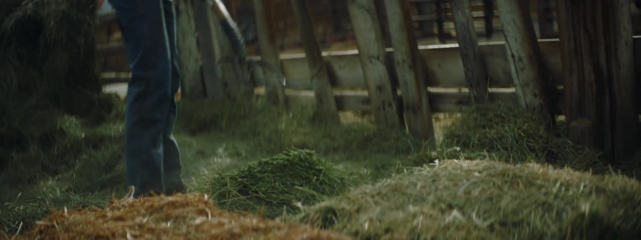 A person moving hay with a pitchfork in a barn