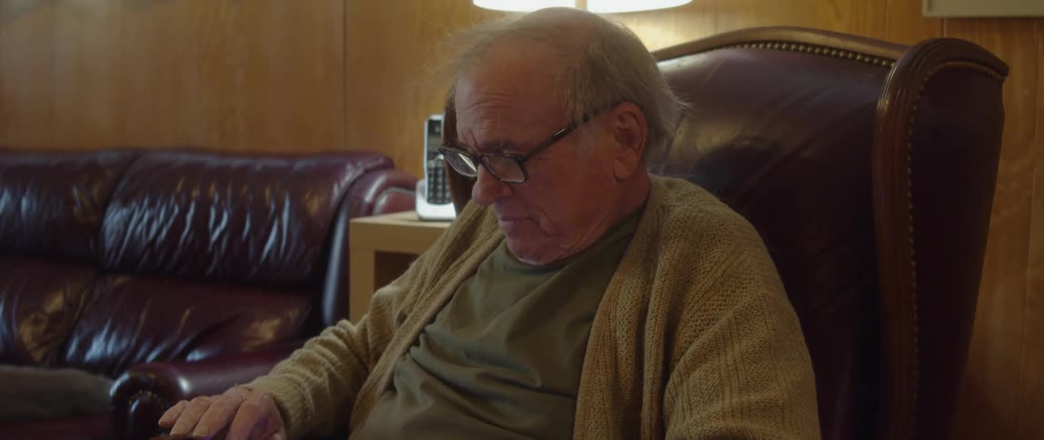 Senior man sitting in easy chair in living room playing a game on smartphone