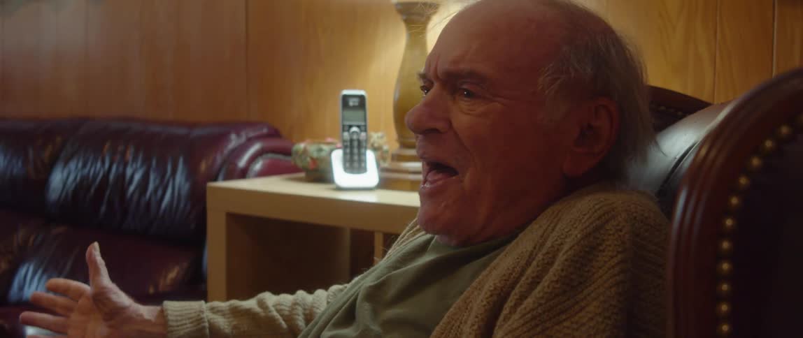 A man sitting in a chair says goodbye to someone on the phone and then bursts out in joy