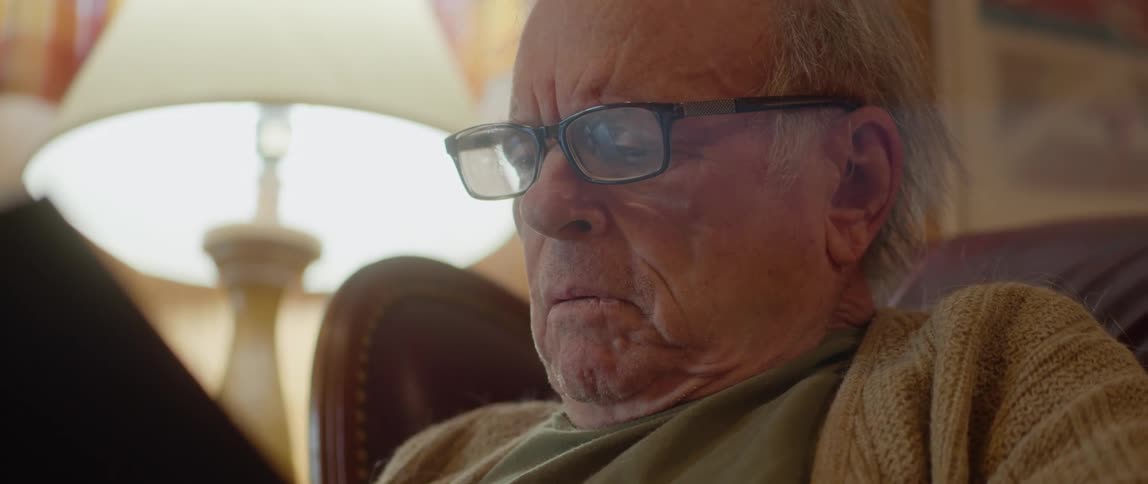 Old man sitting in a chair reading a book that is very concerning