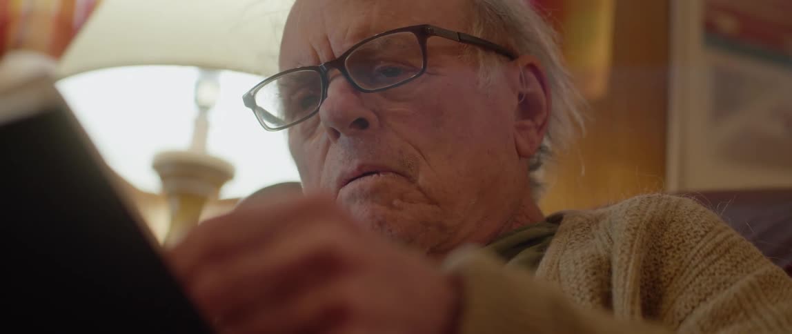 Elderly man sitting in chair reading a book turning the page looks very engaged