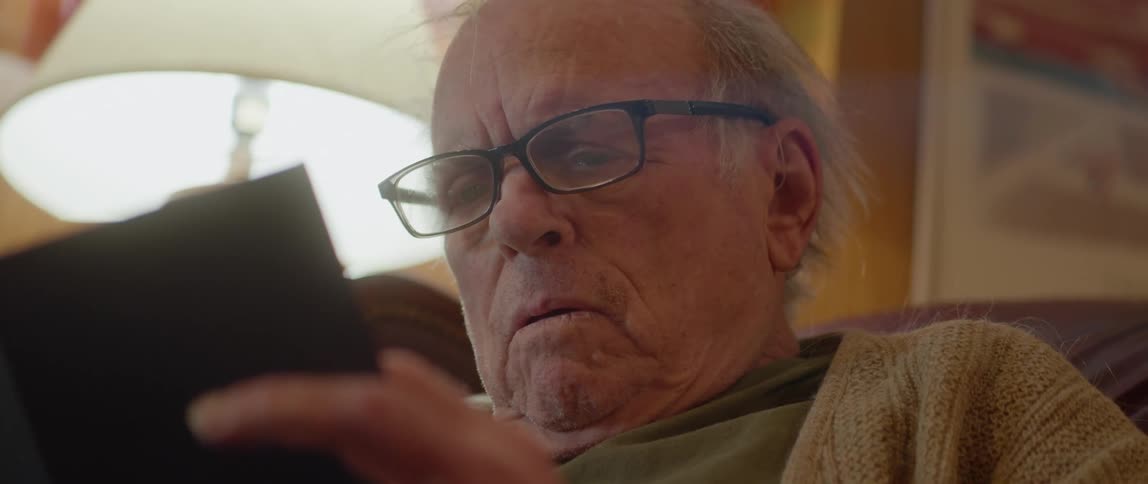 Old man leans back in chair while reading a book and then turns page very engaged