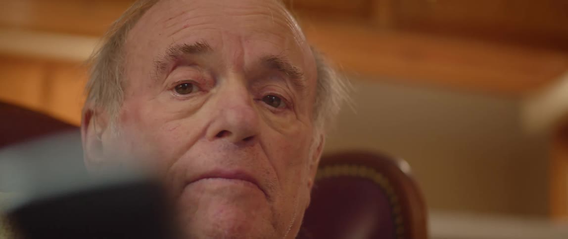 Elderly man sitting in brown armchair answers phone in room