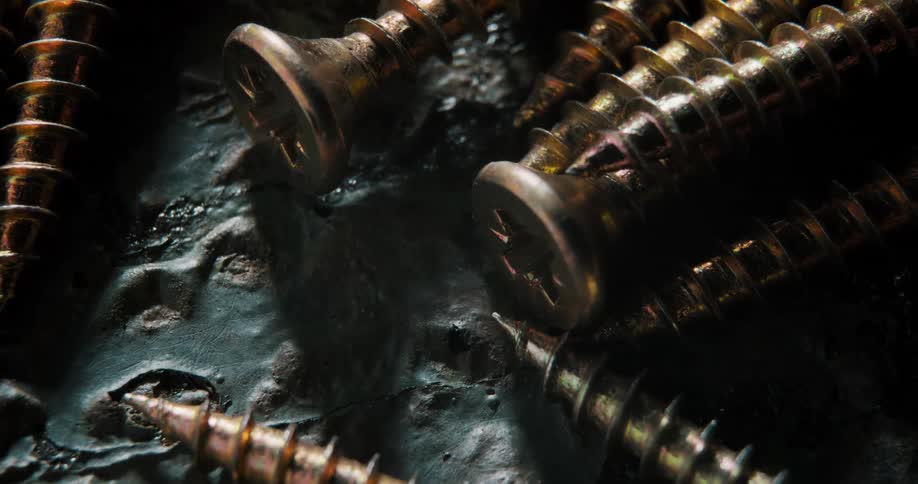 Closeup moving across a few phillips head screws some copper some steel sitting on an imperfectly textured metal surface