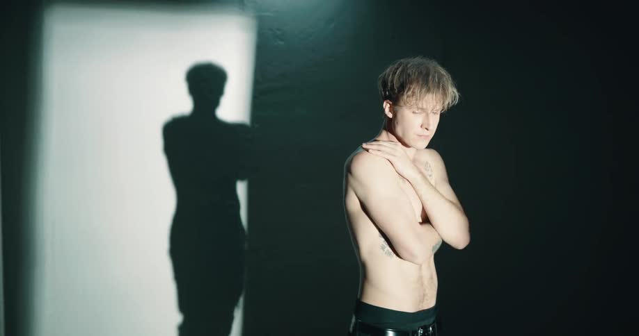 A man stands shirtless in the dark room