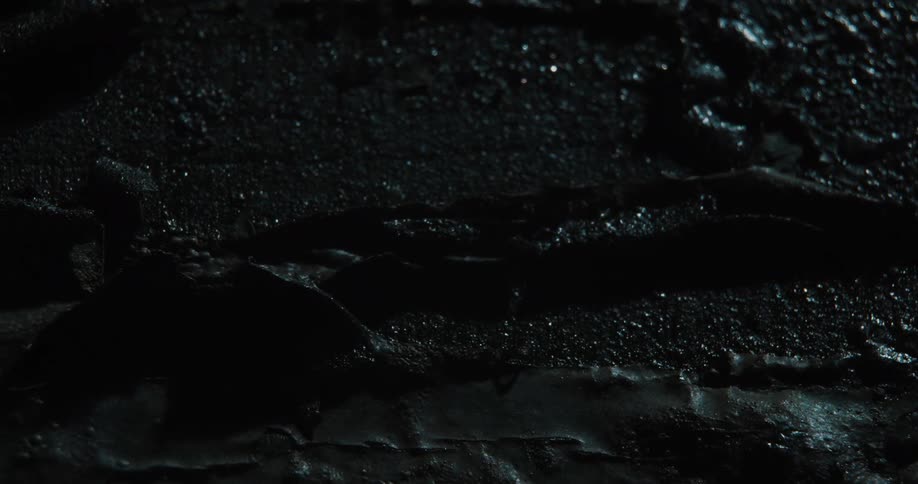 Moving across a closeup of wet broken asphalt and dark metal