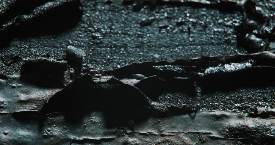 Fade in and out on closeup of textured wet broken asphalt with metal and dark paint