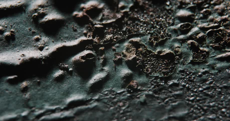Light and shadow move across close up of asphalt texture mixed with broken bits of metals tar and paint