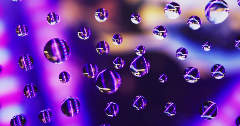 Purple and pink lights move behind water droplets on clear glass with an amber light in the distance