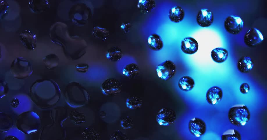 Water droplets sit on clear glass as blue and purple light shines in the distance reflecting on the drops
