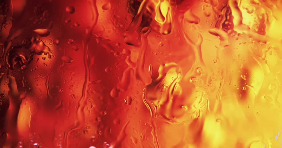 Extreme closeup of glass with water droplets and condensation dripping from it and a red and yellow light behind it
