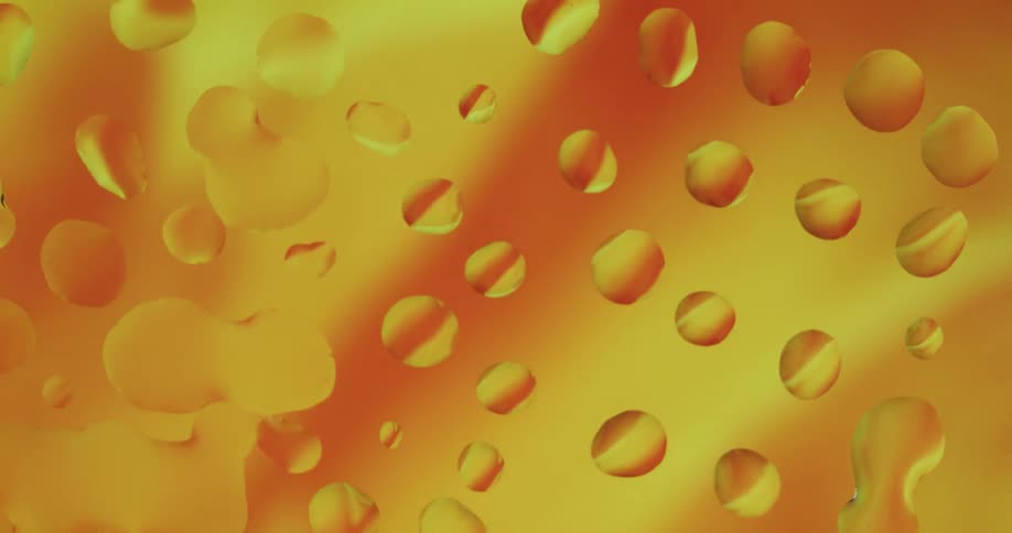 Close up of abstract orange liquid flowing behind a glass with water droplets