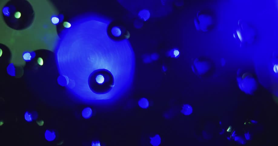 Water droplets sit on clear glass as rotating colored lights move in the distance reflecting on the drops