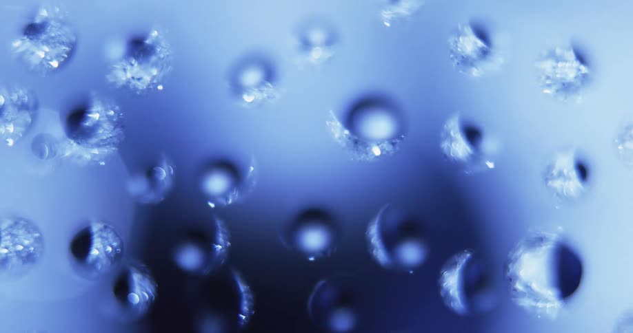 Blue light shines on water droplets as they appear to turn and rotate as texture is reflected inside from the moving light