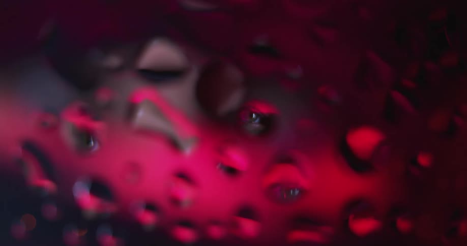 Extreme closeup of water droplets or clear resin on glass reflecting the red light behind it alternating between shadow and light