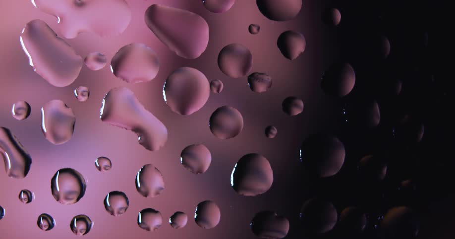 Closeup of water droplets or clear resin on glass reflecting the pink light source behind behind it