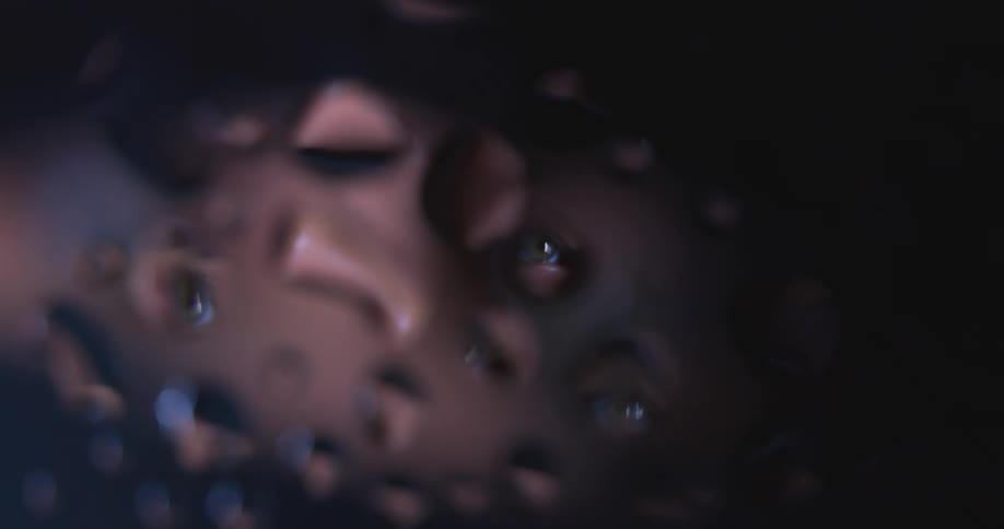 Water droplets sit on clear glass as red lights move in the distance reflecting on the drops