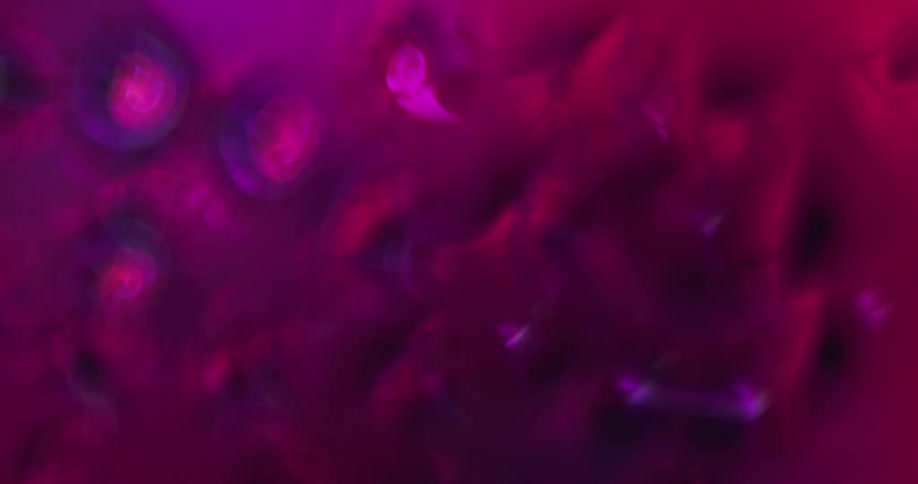 Water droplets sit on clear glass as red and pink light shines as the liquid moves and vibrates