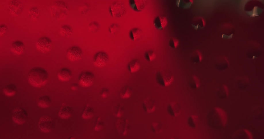 Water droplets sit on clear glass as red lights move in the distance reflecting on the drops