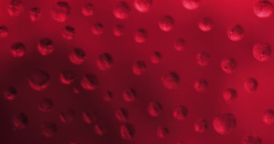 Water droplets sit on clear glass as red lights move in the distance reflecting light and shadows on the drops