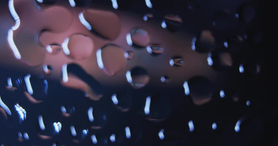 Water droplets are on clear glass as pink light with eyes moves behind them