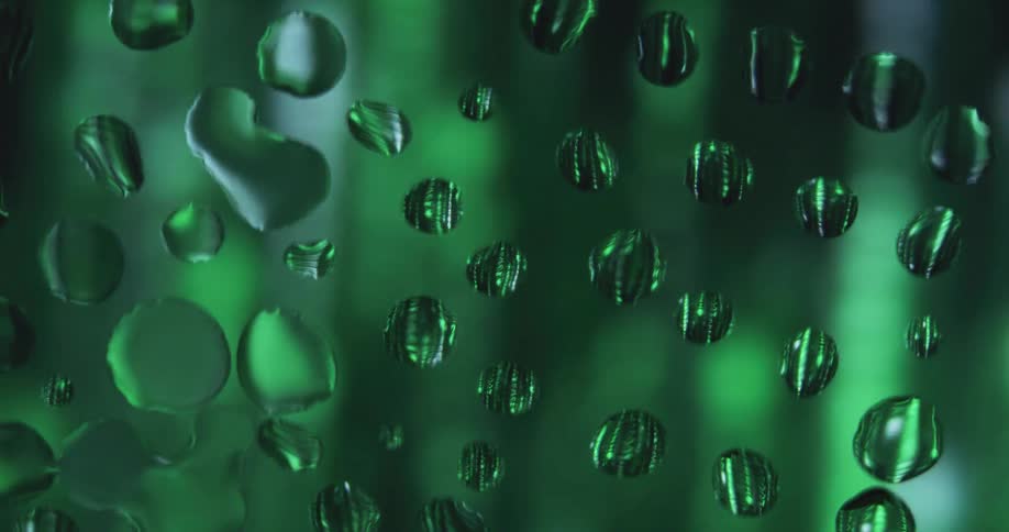 Water droplets are on clear glass as green light moves behind them