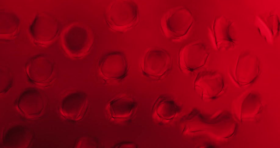 Water droplets sit on clear glass in the darkness as a red light shines texture develops inside the drops