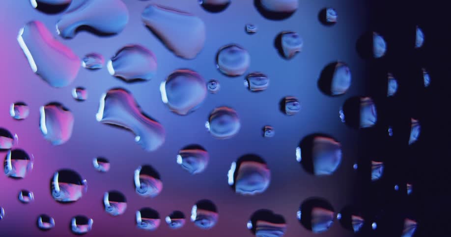 Water droplets sit on clear glass as purple and pink light shines behind them