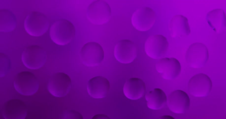 Water droplets sit on clear glass as the color of shining lights change as they reflect in the drops