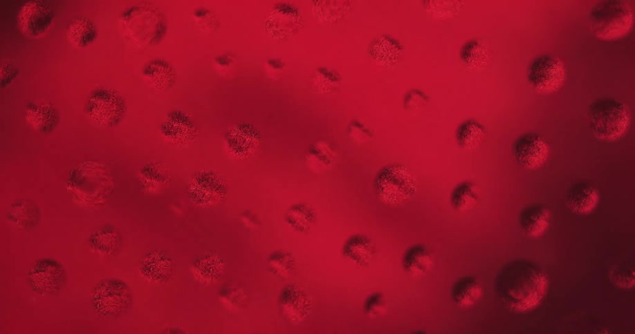 Water droplets sit on clear glass as red lights move in the distance reflecting light and shadows on the drops