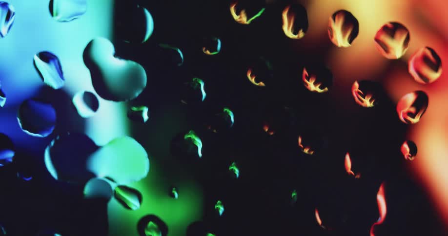Water drops on glass magnify bright flowing colors